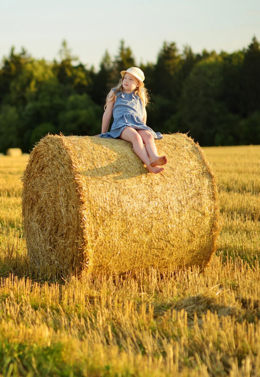 Young girl on round hay bale in the middle of a field in Terrell, TX near Northspur