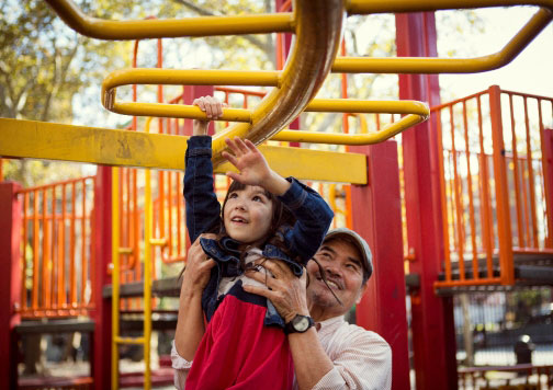 Child doing monkey bars on playground with grandfather